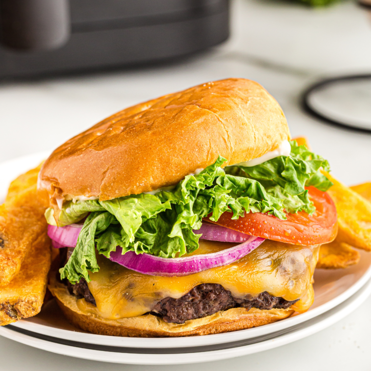 "Close-up of a perfectly cooked bacon cheeseburger made in an air fryer, topped with fresh lettuce and tomato."