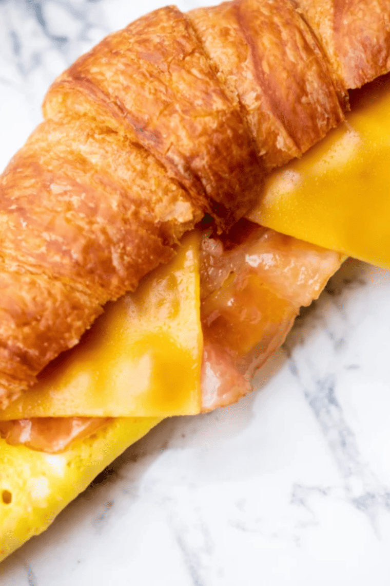 Air fryer bacon egg and cheese croissant cut in half showing candied bacon, a fried egg, and melted cheese.