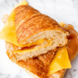 Air fryer bacon egg and cheese croissant cut in half showing candied bacon, a fried egg, and melted cheese