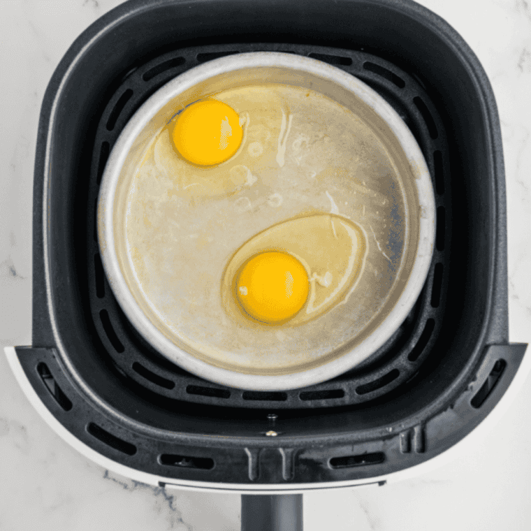 Raw eggs cracked into ramekins in the air fryer basket before cooking
