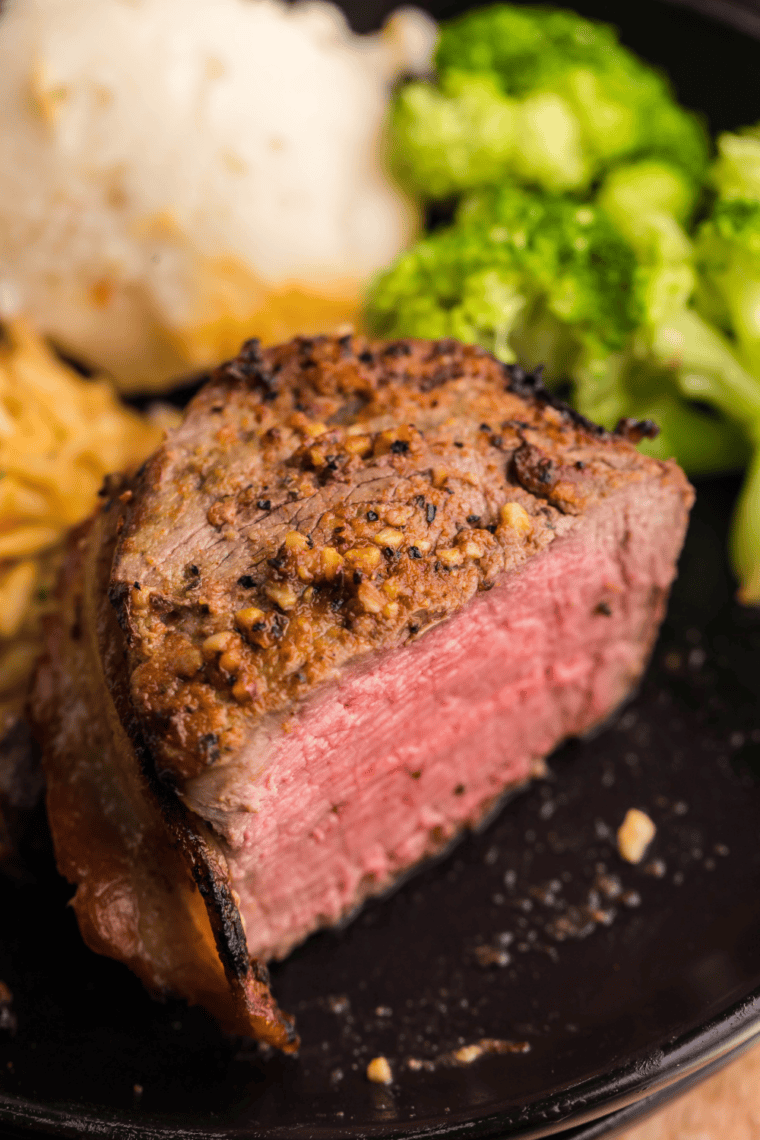 Air fryer bacon-wrapped filet mignon on a plate, crispy bacon exterior with juicy, tender steak inside.