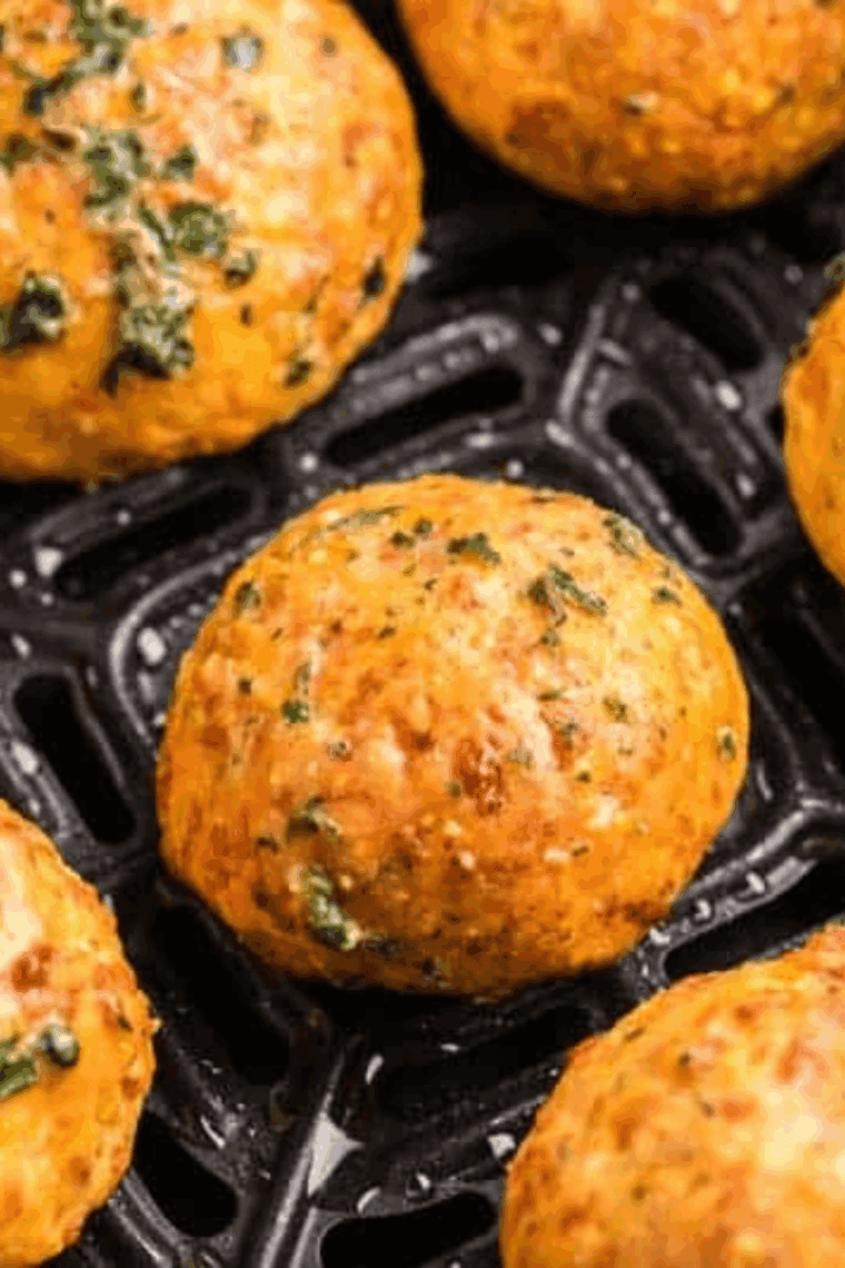 Freshly baked Red Lobster-style cheddar biscuits in an air fryer basket, topped with melted butter and parsley.
