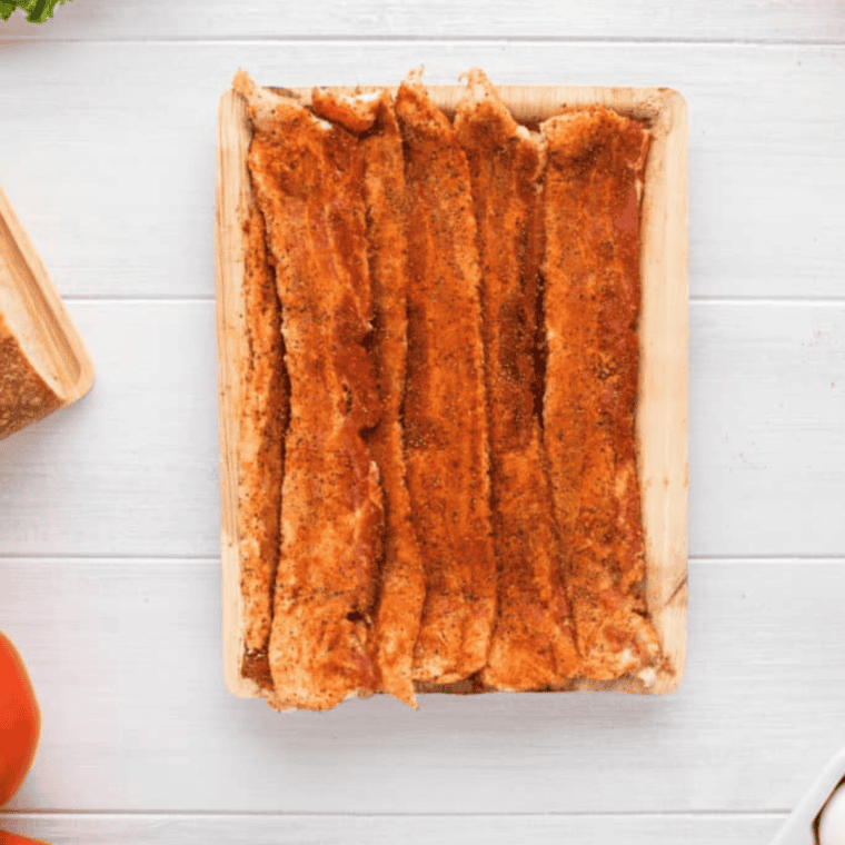 Air fryer basket filled with bacon strips cooking at 400°F for 10-12 minutes, flipped halfway for even crisping, with optional maple syrup brushed on for added flavor.