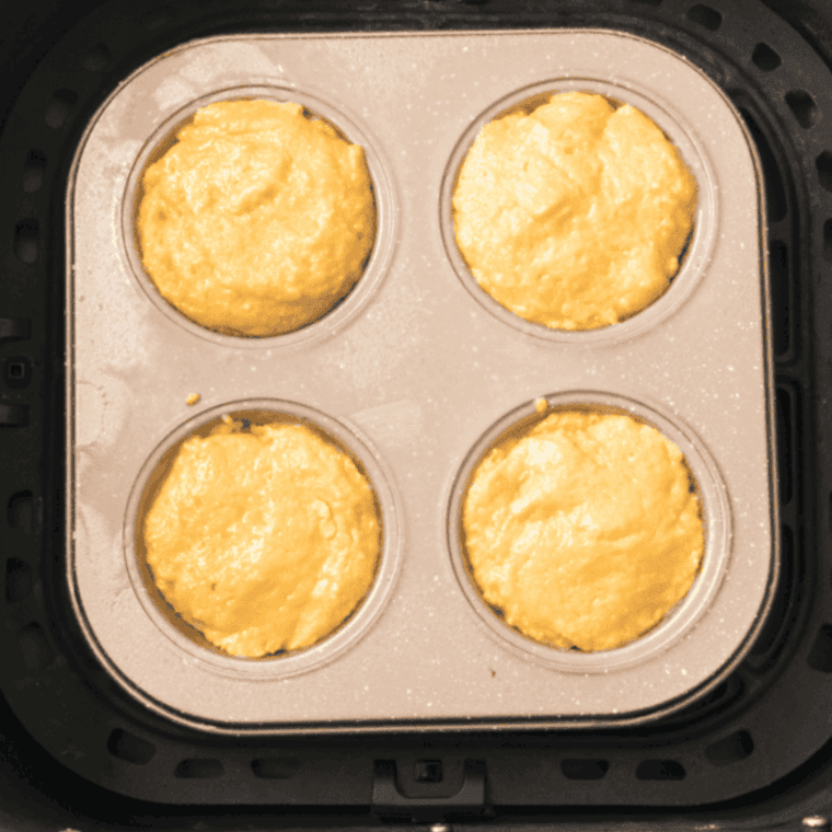 Cornbread batter spooned into cups and placed in an air fryer basket to bake.