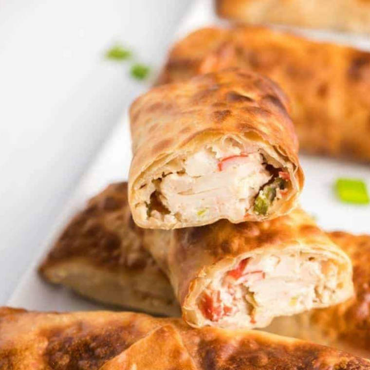 A plate of crispy Air Fryer Crab Rangoon Egg Rolls served with sweet chili sauce for dipping.