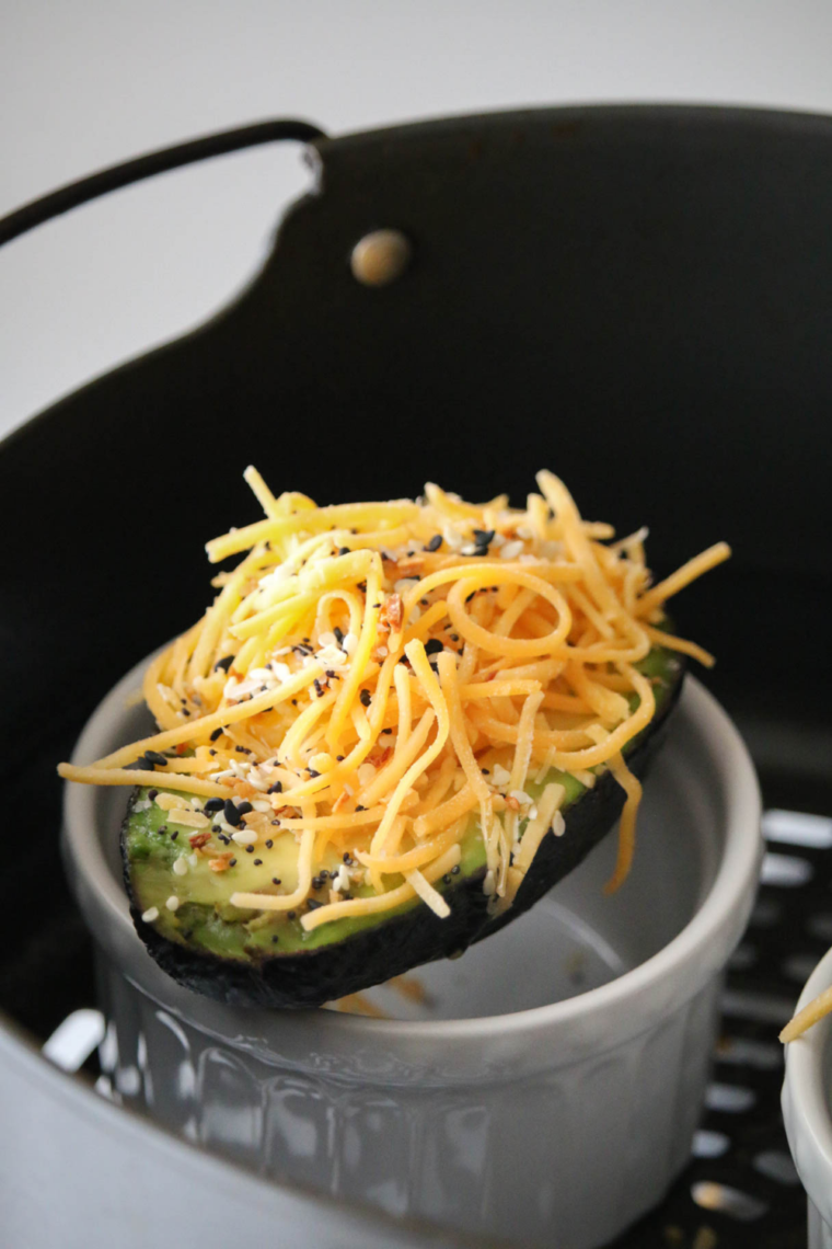 closeup: air fryer avocado egg with cheese and seasonings before air frying