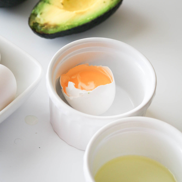 closeup: a cracked egg with a yolk in a white ramekin for air fryer avocado egg