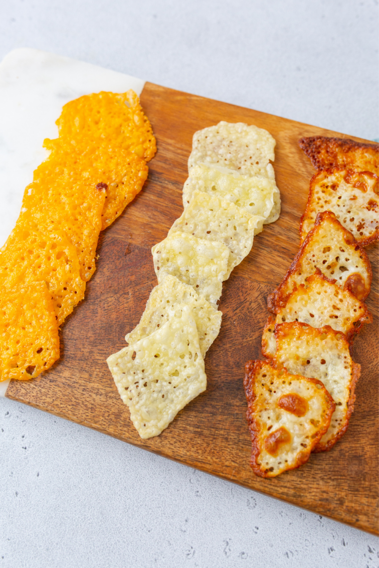 Three types of air fryer cheese crisps on a wooden board &mdash; cheddar, Parmesan, and pepper jack