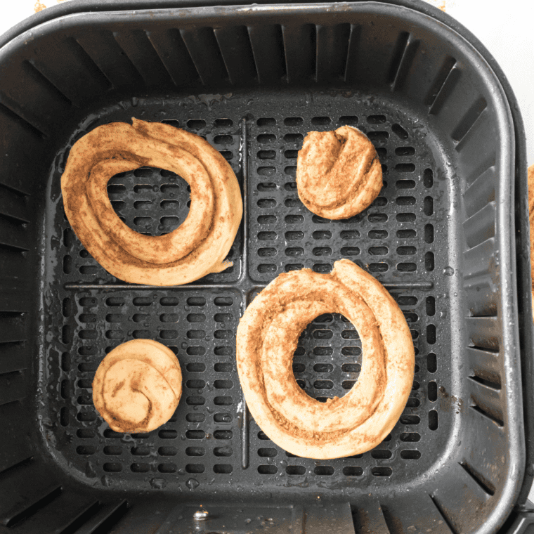 Cinnamon roll donuts arranged in a single layer in the air fryer basket, ready to cook at 320°F