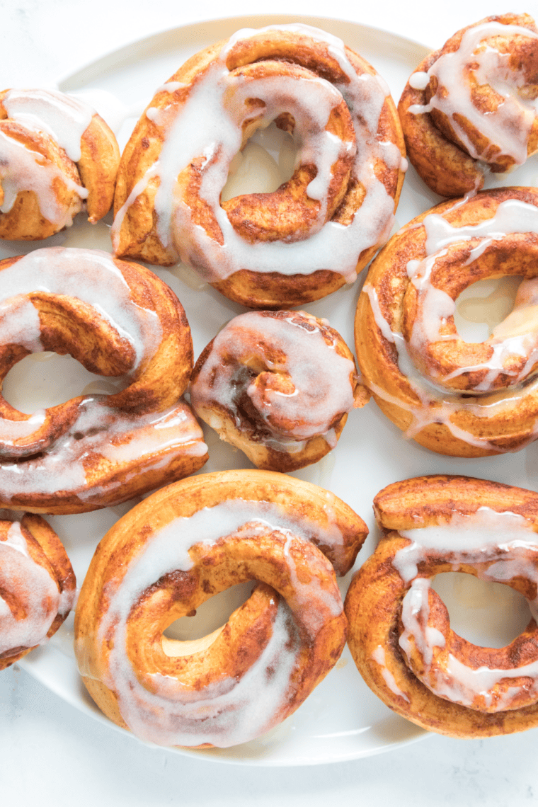 Air fryer cinnamon roll donuts with golden edges and icing drizzle, served warm on a white plate