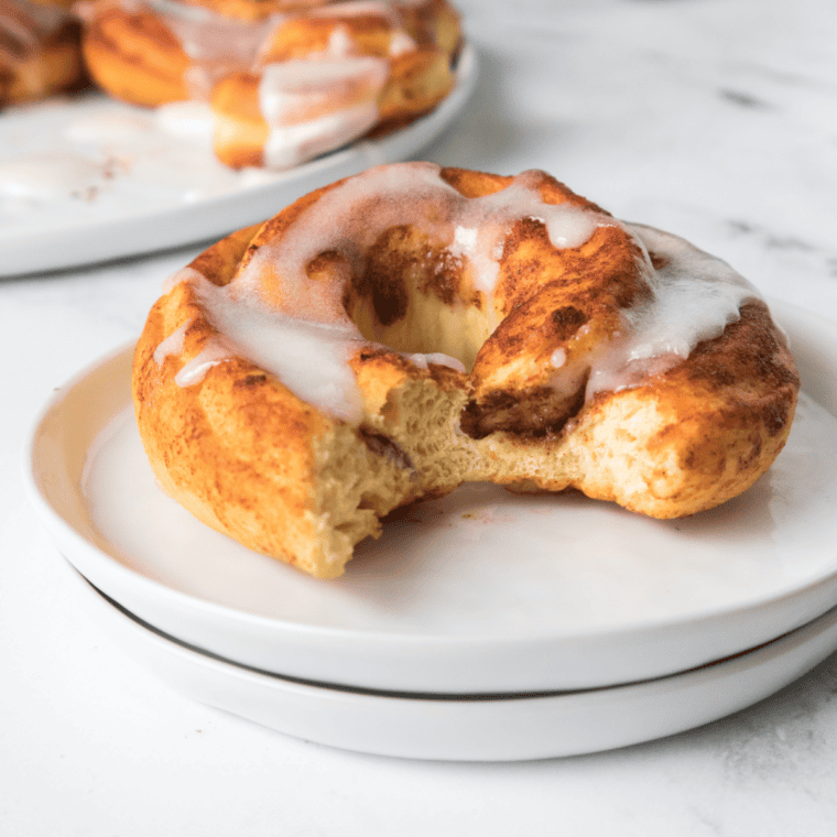 Fluffy air fryer cinnamon roll donuts drizzled with icing, served warm on a white plate