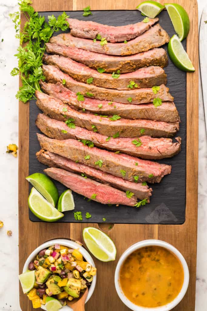 overhead: sliced air fryer flank steak on a slate and wood cutting board with salsa and orange sauce to the side