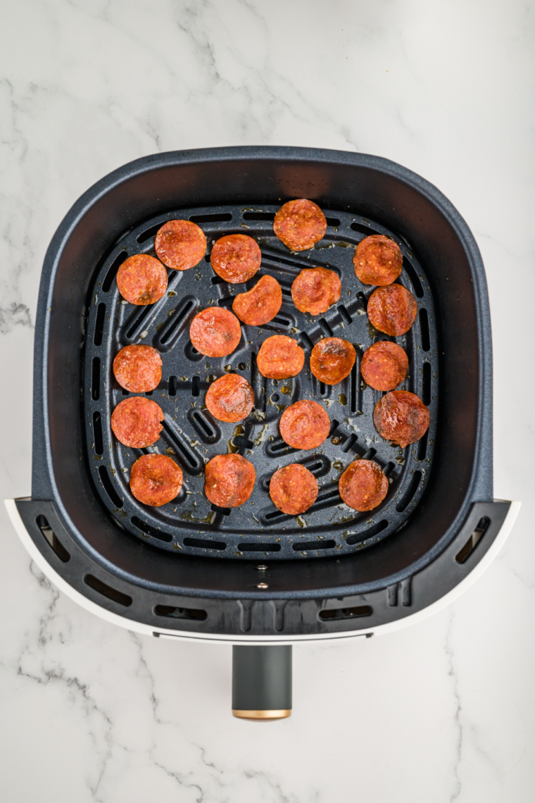 Air fryer with pepperoni chips cooking inside.