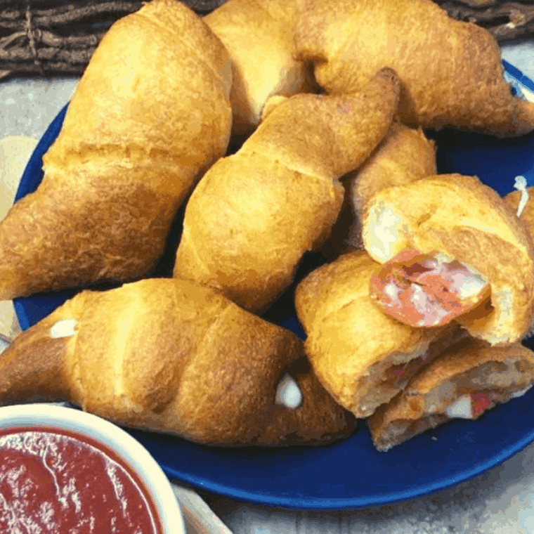 Golden air fryer crescent rolls stuffed with pepperoni and melted cheese, served with a side of pizza sauce.