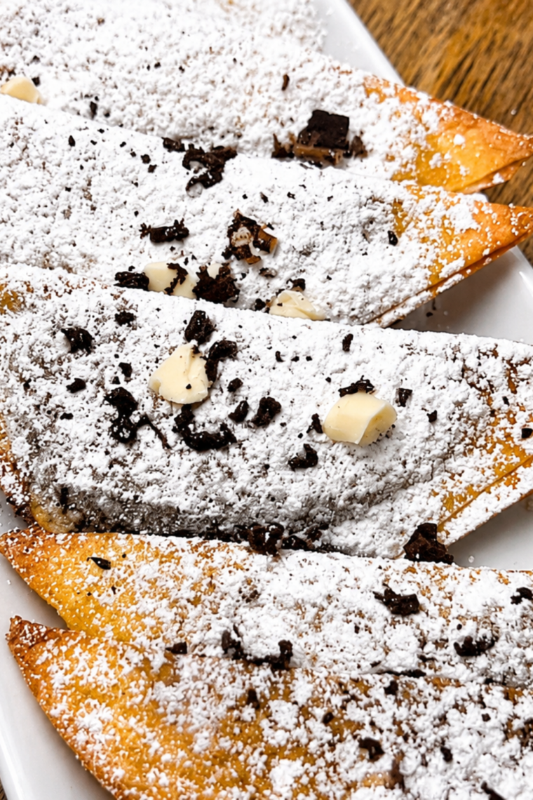 Crispy air fryer Nutella wontons dusted with powdered sugar, one broken open showing the molten chocolate center