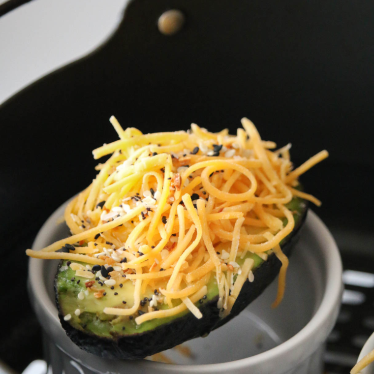 closeup: avocado egg in the air fryer with cheese and seasonings on top before air frying