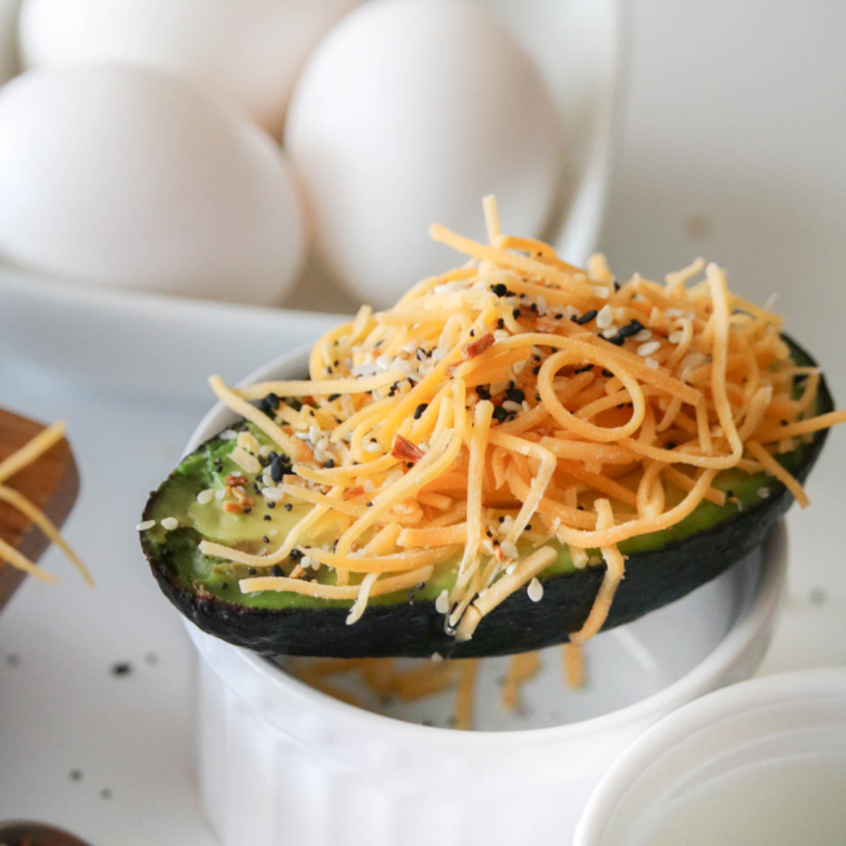 closeup: shredded cheese and seasonings on top of an avocado egg in air fryer before cooking