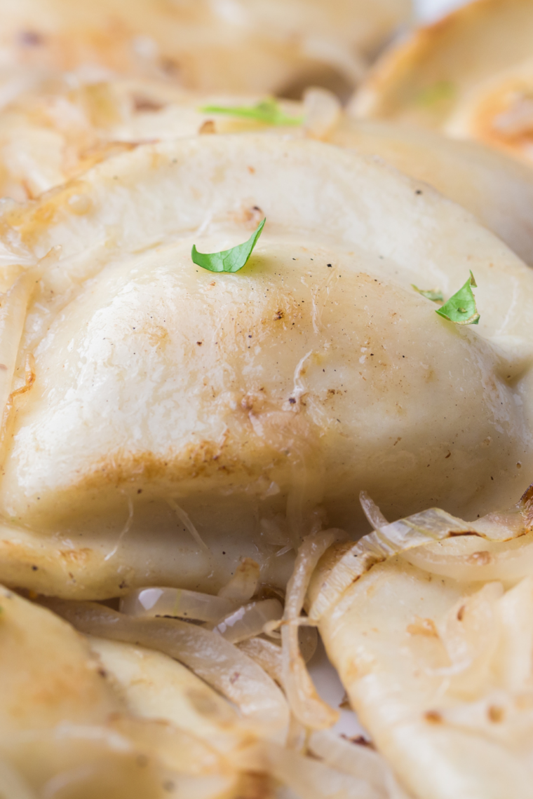 Golden-brown air fryer pierogies topped with caramelized onions, served on a plate.