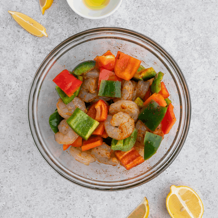 Prep the Shrimp and Peppers: Shrimp and colorful bell peppers tossed with olive oil, garlic powder, smoked paprika, salt, and chili flakes in a large bowl.