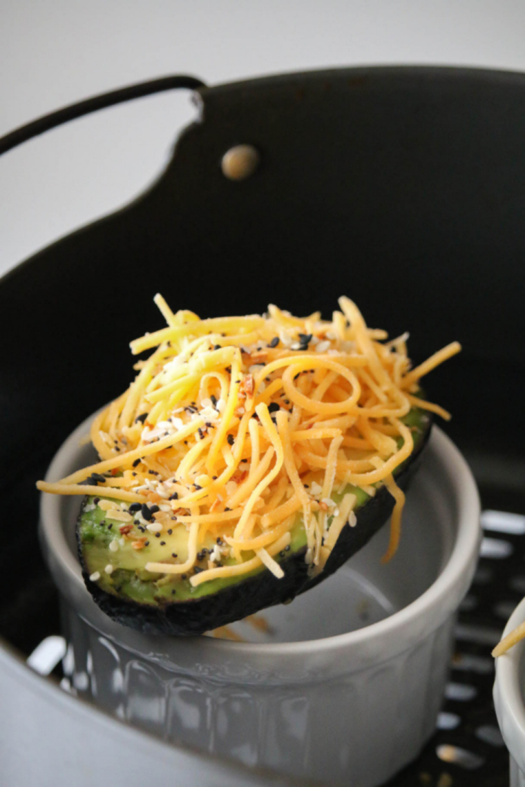 Air fryer avocado halves filled with perfectly cooked eggs, garnished with fresh herbs, served on a plate.