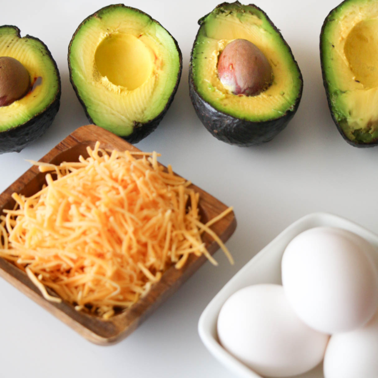 closeup: avocado halves, shredded cheddar, and raw eggs for my egg in avocado air fryer recipe