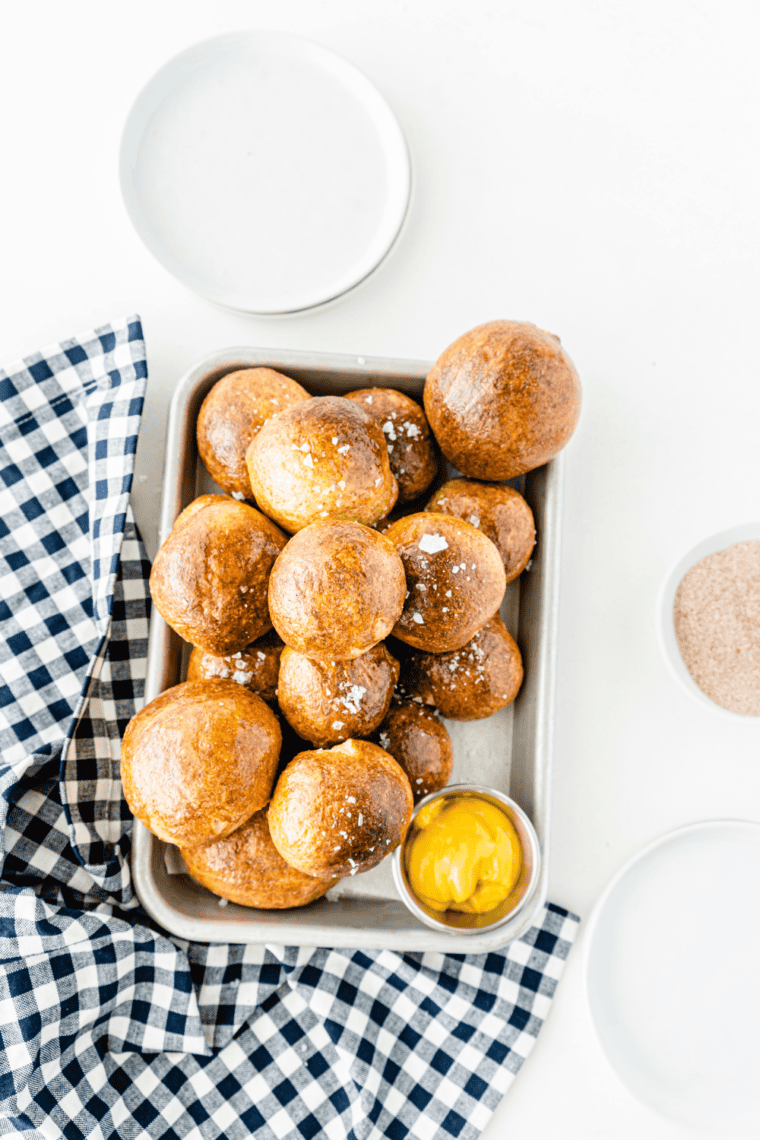 Close-up of golden pretzel bites on a plate served with cheese dipping sauce and mustard for a soft, chewy appetizer snack.