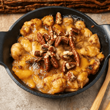 Air fryer cinnamon roll peach cobbler in a cast iron pan with icing drizzled over the golden top