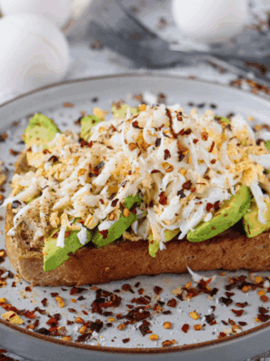A plate of golden, crispy Air Fryer Avocado Toast topped with mashed avocado and garnished with seasonings.