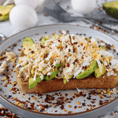 A plate of golden, crispy Air Fryer Avocado Toast topped with mashed avocado and garnished with seasonings.