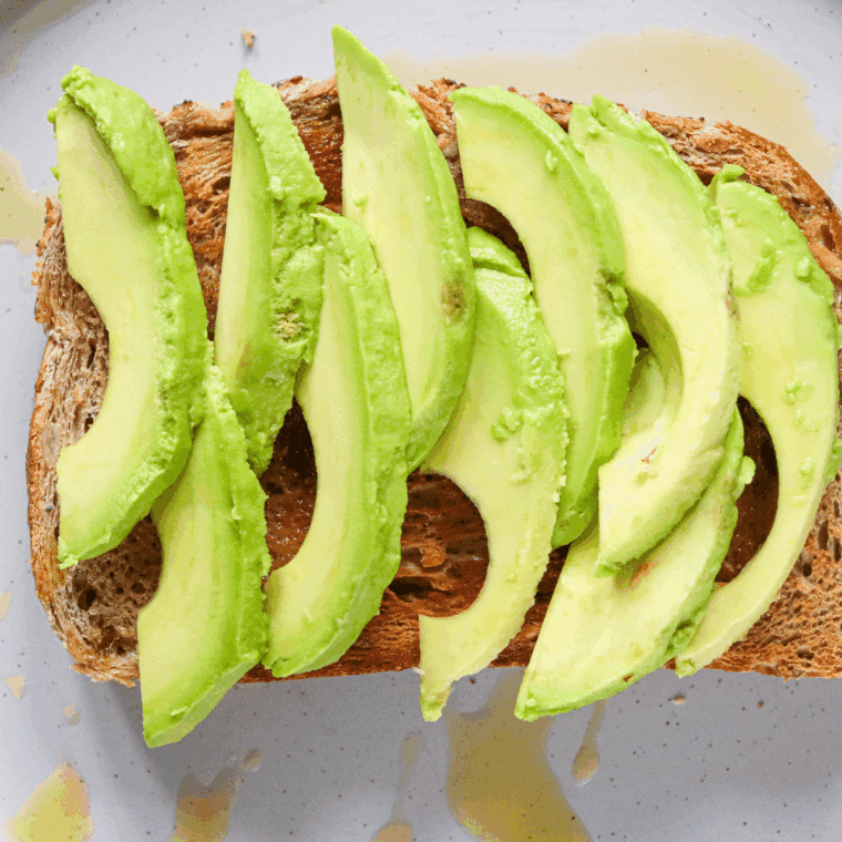 Piece of toast on plate with sliced avocado pieces.