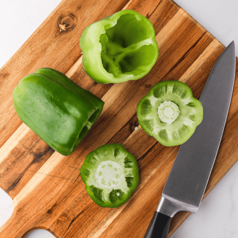 Slicing the tops off bell peppers and removing seeds to create hollow "cups" for stuffing.