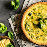 Slice of air fryer broccoli cheddar quiche on a white plate with a golden, flaky crust
