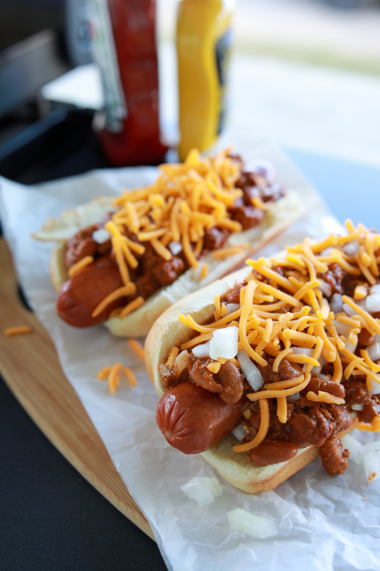 Air Fryer Chili Cheese Hot Dogs topped with melted cheese and chili, served in soft hot dog buns on a plate