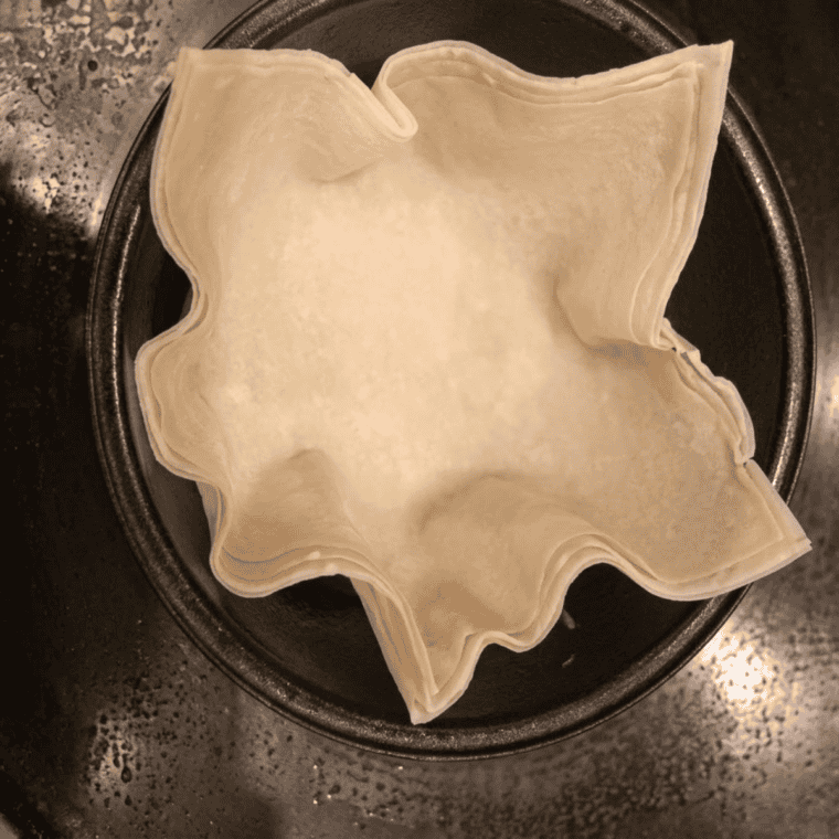 Pressing a wonton wrapper into a greased muffin tin cup