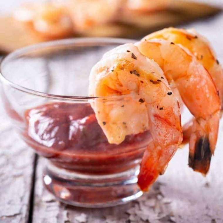 Shrimp dipped into tangy cocktail sauce - Shrimp being dipped into a bowl of cocktail sauce, ready to eat.