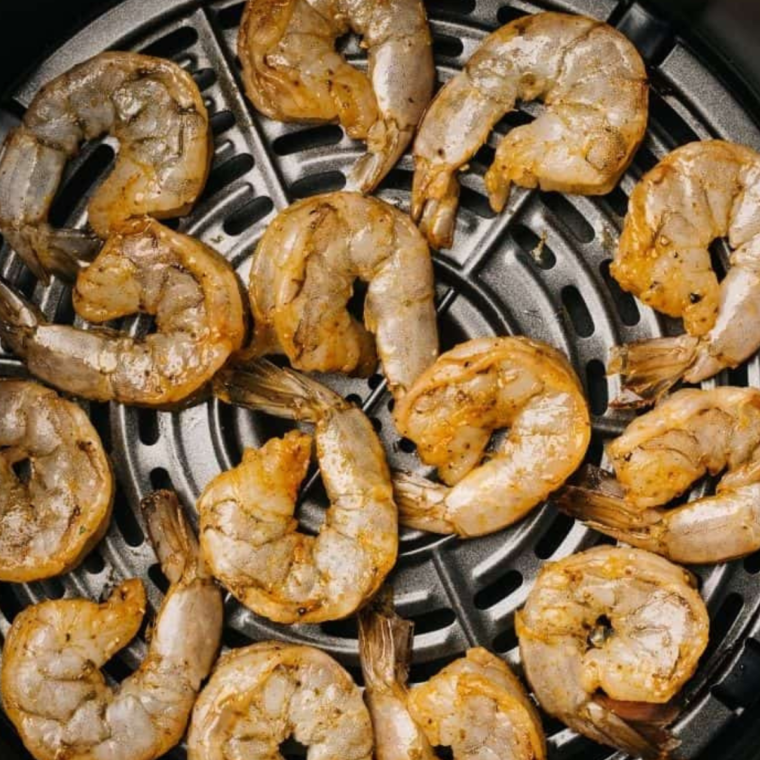 Arranging seasoned shrimp in the air fryer basket - Shrimp placed in a single layer inside the air fryer basket.