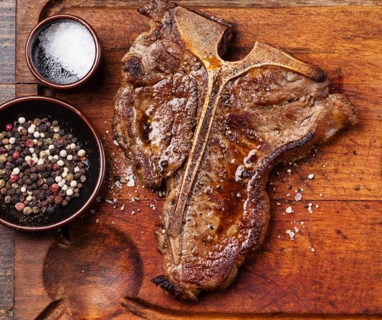 air fryer t bone steak on a chopping board with salt and pepper