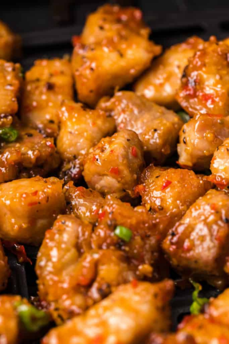 Golden crispy pork belly pieces coated in spicy ginger sauce served in a bowl with fresh herbs.