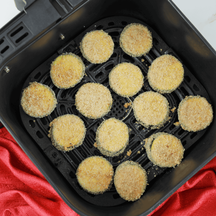 Breaded zucchini sticks arranged in air fryer basket cooking until crispy