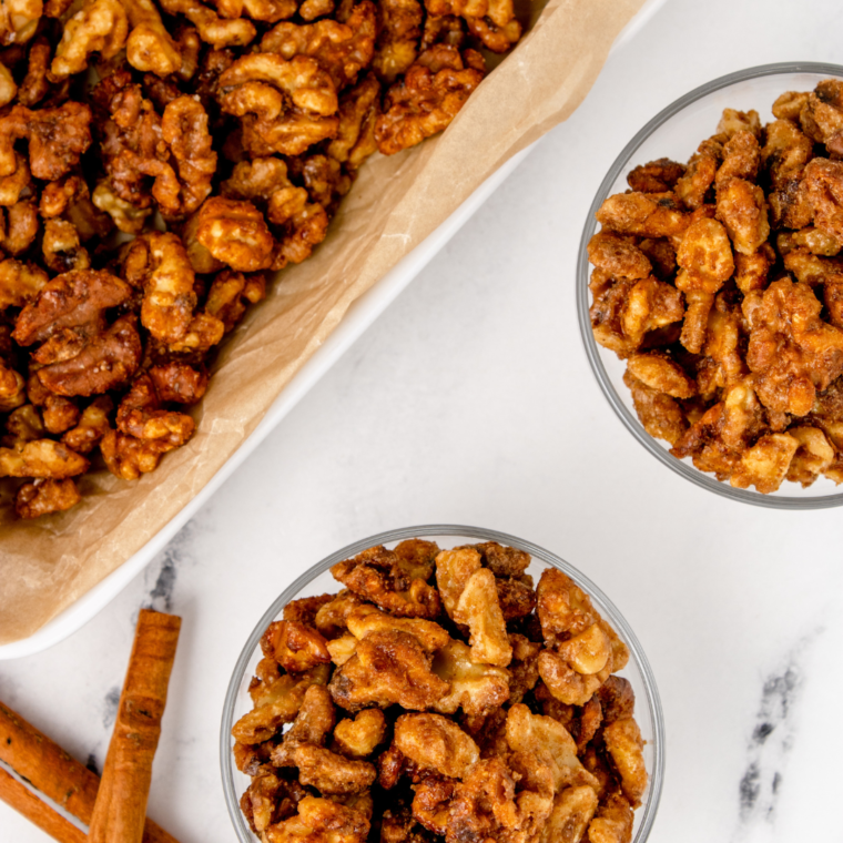 overhead closeup: 2 bowls of air fried walnuts with a baking sheet to the side with more