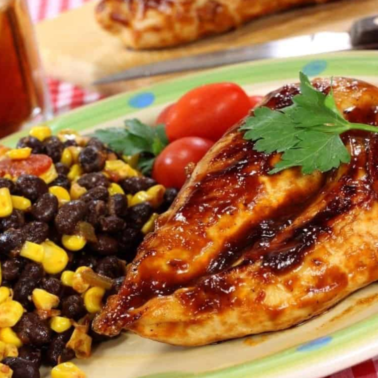 Plate of air fryer bourbon BBQ chicken tenders served with dipping sauce and garnished with herbs.