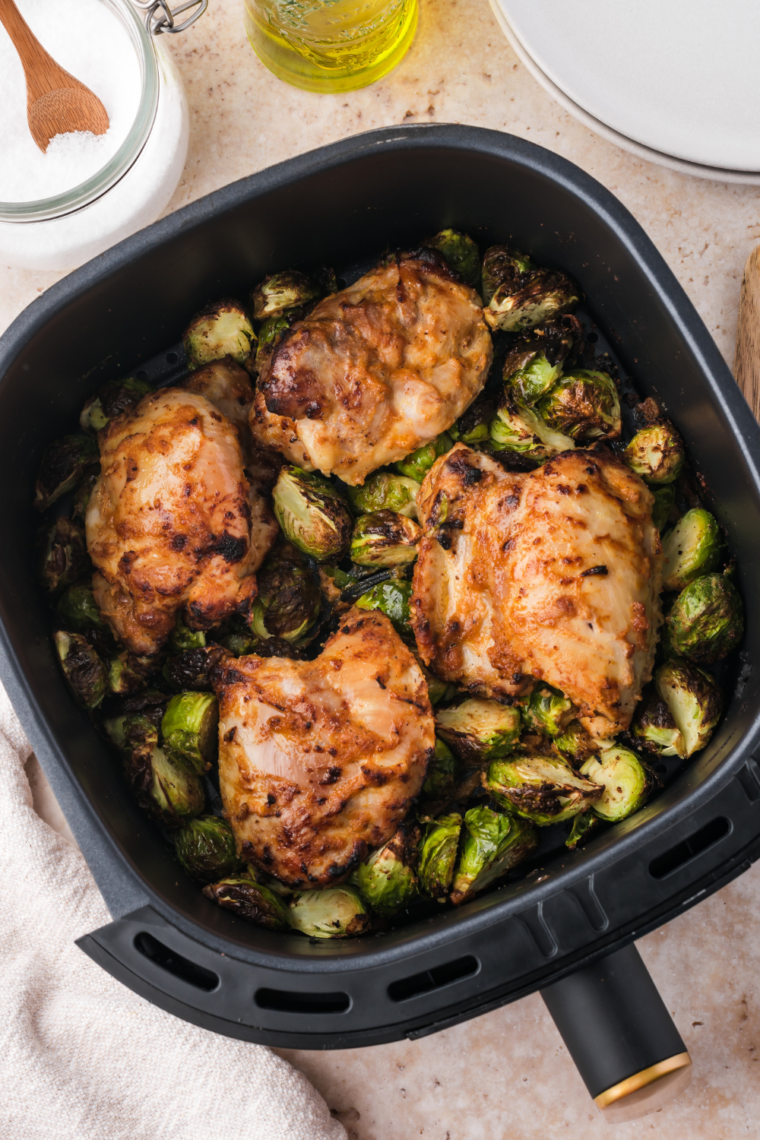 Crispy air fryer honey balsamic Brussels sprouts served alongside golden air fryer chicken thighs on a white dinner plate