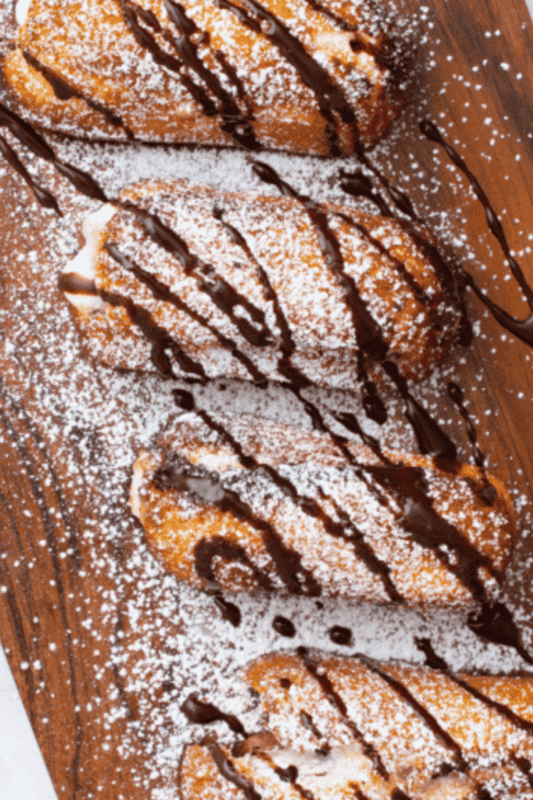 Crispy air fryer Twinkies on a plate, topped with powdered sugar and chocolate drizzle.