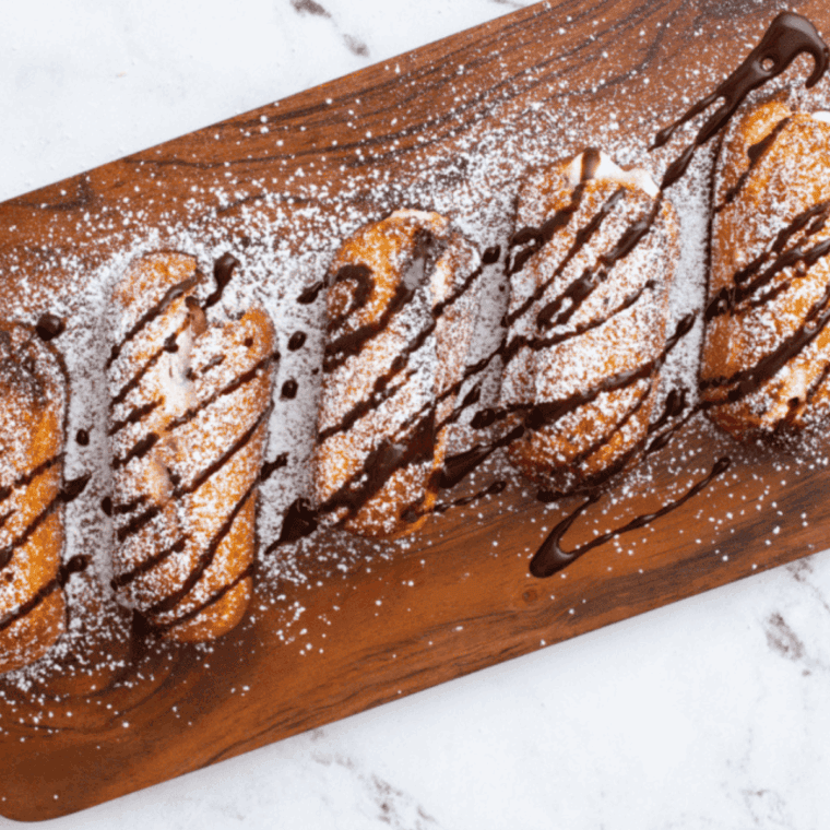 Golden air fryer Twinkies served on a plate with chocolate drizzle and powdered sugar.