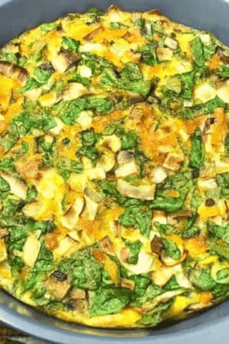 Roasted vegetable frittata sliced on a plate showing fluffy baked eggs with colorful vegetables and melted cheese.