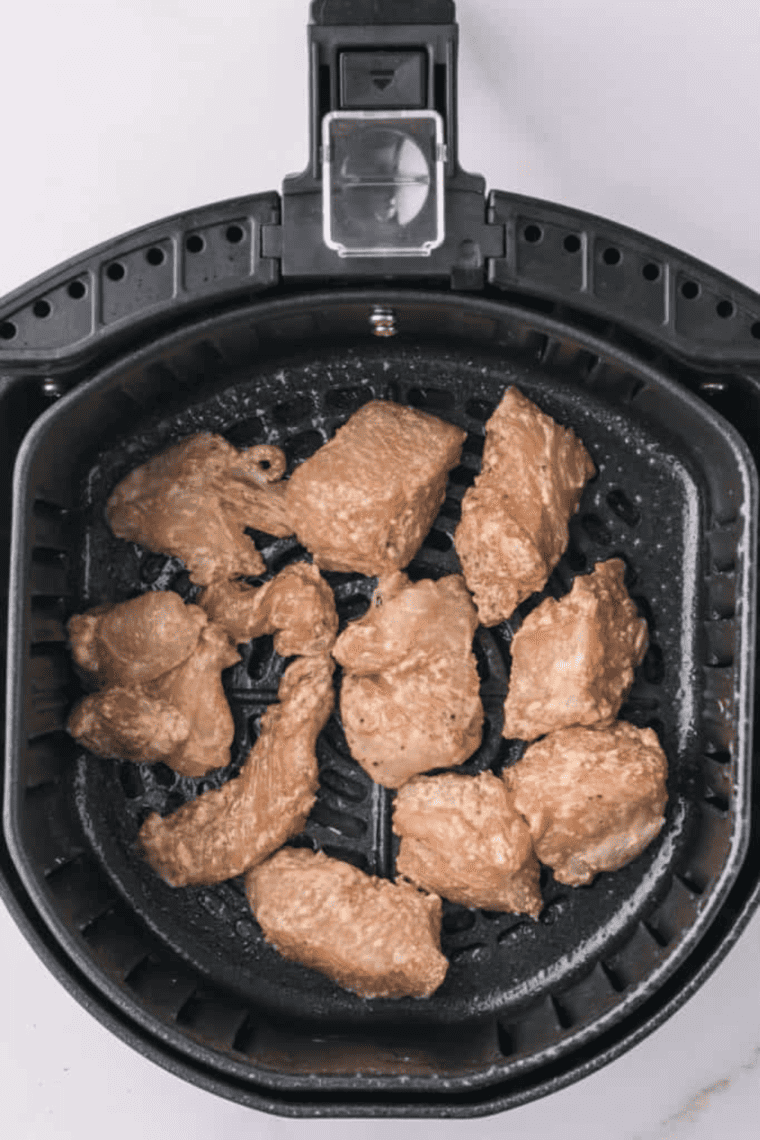 Seasoned diced chicken in an air fryer basket cooking at 350°F until golden and fully cooked.