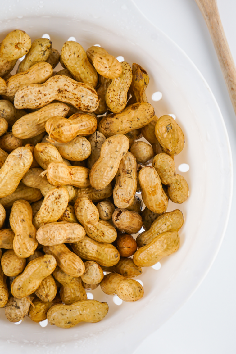 Season the Peanuts: Peanuts in a bowl being tossed with salt and seasonings.