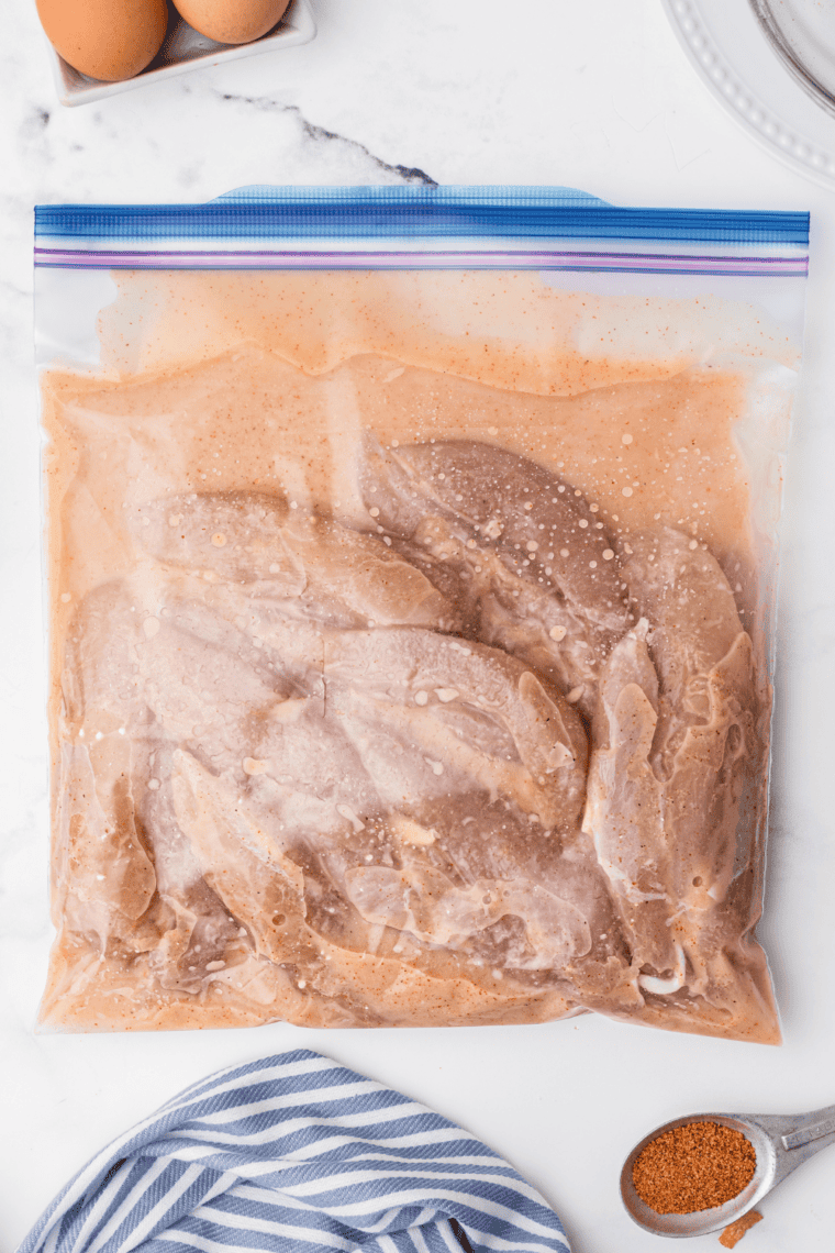 Seasoning chicken and shrimp with chipotle powder, olive oil, and salt in a bowl.