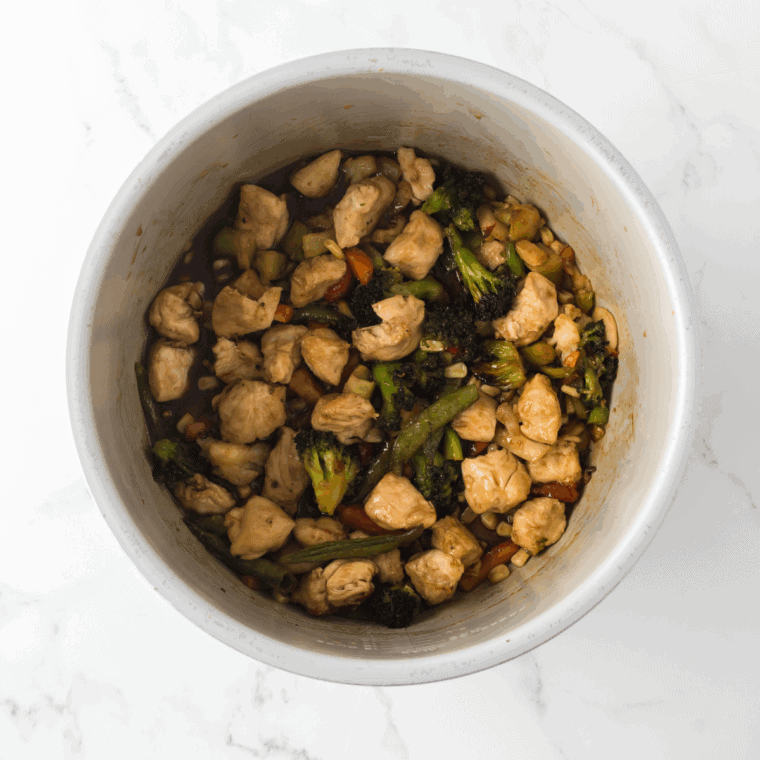 Combine and Saute: Cooked chicken and vegetables in the Ninja Foodi Instant Pot with sauce, simmering and thickening.