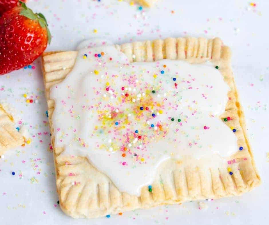 Homemade Air Fryer Pop Tart finished and covered in sprinikles. The tart is sitting on a white counter with some extra strawberries next to it.